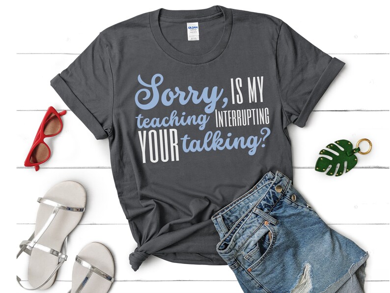 May include: A dark grey t-shirt with the text "Sorry, is my teaching interrupting your talking?" in white and blue lettering.