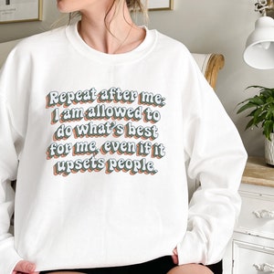 May include: White sweatshirt with the text "Repeat after me, I am allowed to do what's best for me, even if it upsets people." in a retro-style font.