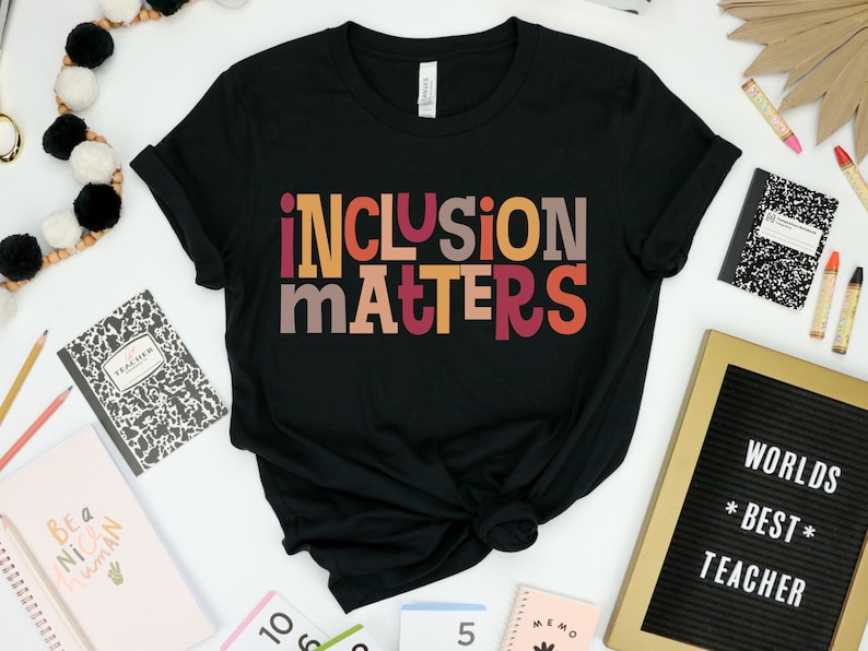 Puede incluir: Camiseta negra con el texto "inclusion matters" en letras de bloque de colores. Las letras son en tonos de rojo, naranja, amarillo y marr&oacute;n.