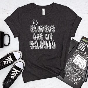 May include: A dark gray t-shirt with white text that reads "ELOPERS ARE MY CARDIO". The text is in a bold, blocky font.