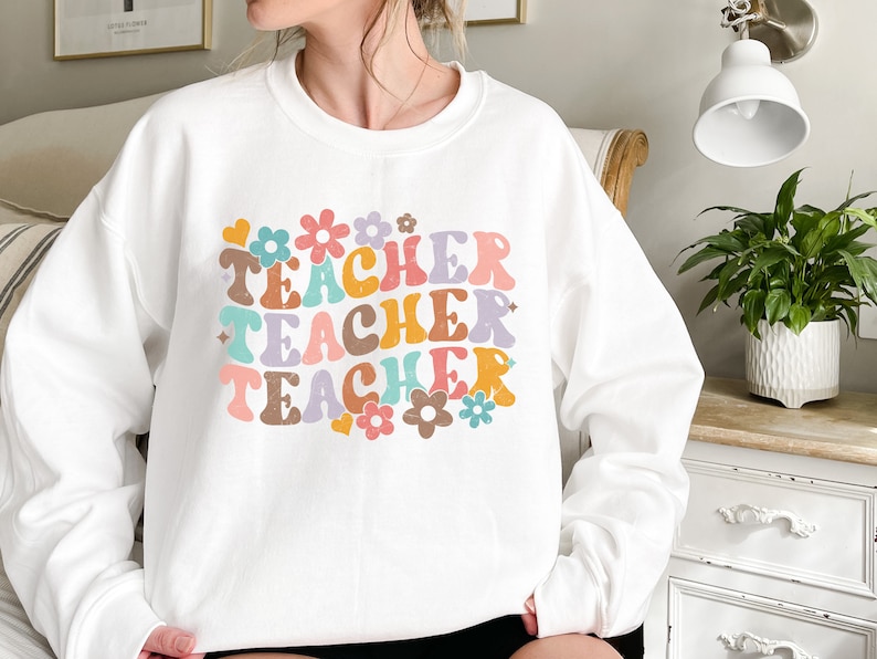 May include: White sweatshirt with the words "Teacher Teacher Teacher" in colorful retro font with flowers and hearts around the text.