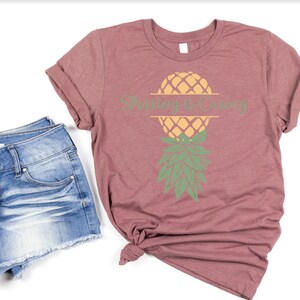 Puede incluir: Una camiseta color malva con un gr&aacute;fico de pi&ntilde;a y el texto "Sunny is Calling". La camiseta se combina con pantalones cortos de mezclilla.