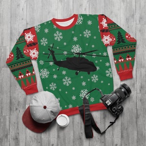 May include: Green Christmas sweater with a black silhouette of a helicopter and a snowflake pattern. The sweater has red trim and red and black patterned sleeves.