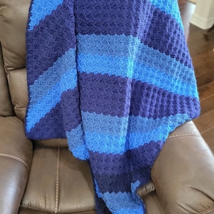 May include: A blue and navy striped crocheted throw blanket draped over a brown leather armchair.