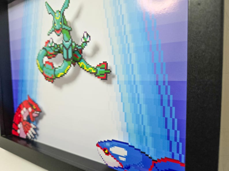 Puede incluir: Una pieza de arte de p&iacute;xeles enmarcada con tres personajes de Pok&eacute;mon: un Pok&eacute;mon de tipo agua verde y azul, un Pok&eacute;mon de tipo fuego rojo y negro y un Pok&eacute;mon de tipo agua azul y blanco. El fondo es un dise&ntilde;o pixelado azul y blanco.