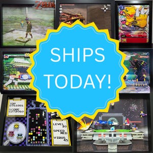 May include: A collection of six black shadow box frames displaying various video game and trading card scenes, including The Legend of Zelda, Agumon, Street Fighter, Umbreon, Dr. Mario, and a Super Smash Bros stage, arranged in a grid layout.