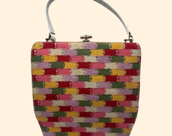 Puede incluir: Un bolso vintage con un colorido patrón bordado. El bolso tiene forma rectangular, un asa blanca y un cierre de broche. El bordado incluye hilos rojos, amarillos, verdes y rosas.