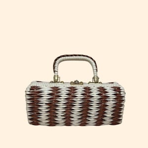 May include: A vintage rectangular wicker handbag with a brown and white chevron pattern. The bag has a white handle with brown accents and gold-colored metal hardware. The clasp is gold-toned.