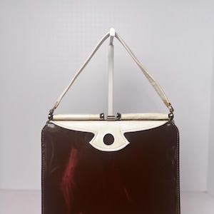 May include: A vintage brown and white patent leather handbag with a gold clasp and a white circle detail on the front.