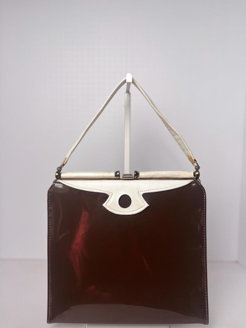 May include: A vintage brown and white patent leather handbag with a gold clasp and a white circle detail on the front.