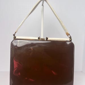 May include: A brown patent leather handbag with a white strap and gold hardware.