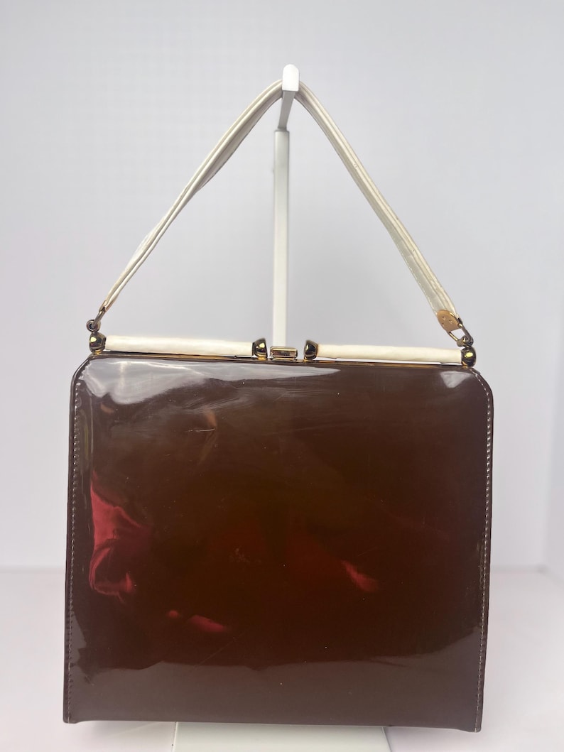 May include: A brown patent leather handbag with a white strap and gold hardware.