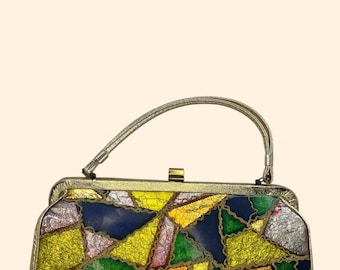 May include: A vintage handbag with a colorful patchwork design. The bag features a variety of colors including blue, yellow, green, pink, and silver. It has a gold-toned frame, a clasp closure, and a thin handle.