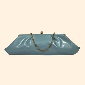 May include: A light blue clutch purse with a gold-colored chain strap. The purse has a shiny, smooth finish and a clasp closure. The design is a classic, elegant style.