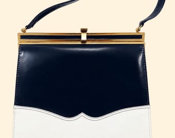 Puede incluir: Un bolso estructurado de diseño bicolor con una sección superior en azul marino oscuro y una sección inferior blanca. El bolso cuenta con un marco de metal dorado, un asa superior única y un cierre central dorado con detalle de costura.