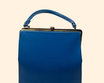 Könnte beinhalten: Eine blaue Vintage-Handtasche mit geschwungenem Griff und goldfarbenem Verschluss. Die rechteckige Tasche hat eine kräftige, blaue Farbe. Der Griff ist ebenfalls blau und oben an der Tasche befestigt.