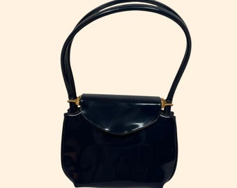 Könnte beinhalten: Eine glänzende, marineblaue Handtasche mit geschwungenem Klappenverschluss und zwei schmalen Henkeln. Die Tasche hat goldfarbene Hardware-Akzente und eine strukturierte Silhouette. Ein klassisches Accessoire.