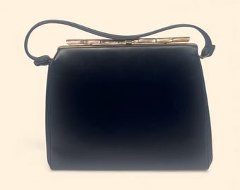 May include: A vintage black handbag with a rectangular shape and a curved handle. The bag features a gold-toned clasp and trim. The handle is attached to the top of the bag with a knot detail. The bag is made of a smooth material.