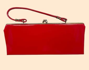 Peut inclure: Une pochette rectangulaire rouge à la finition brillante, dotée d'un cadre en métal doré, d'une fermeture à fermoir pivotant centrale et d'une fine anse rouge fixée sur le dessus par de petites boucles en métal doré.