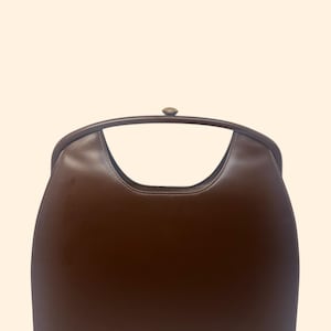 May include: A brown handbag with a curved handle and a clasp closure. The bag has a smooth, glossy finish and a structured shape. The handle is arched, and the bag's body is a solid, rich brown color.