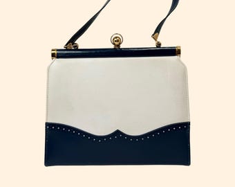Puede incluir: Bolso de mano vintage con cuerpo blanco y sección inferior azul marino. El bolso presenta un diseño curvo con pequeños tachuelas decorativas. Tiene un asa negra y herrajes dorados.
