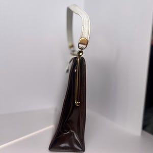 May include: A brown leather handbag with a white strap and a gold clasp.
