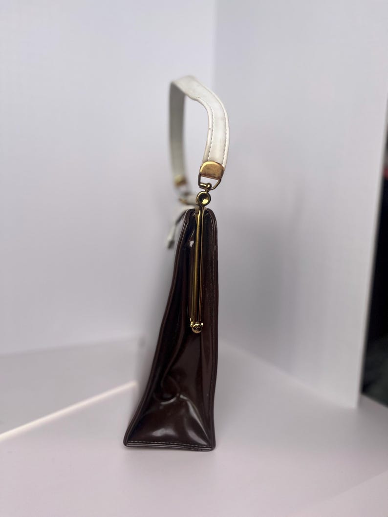 May include: A brown leather handbag with a white strap and a gold clasp.