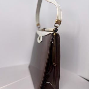 May include: A brown and white vintage handbag with a gold clasp and a white handle.