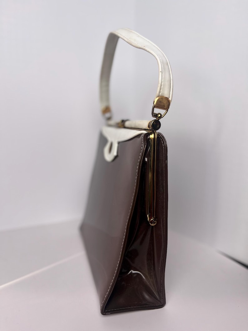 May include: A brown and white vintage handbag with a gold clasp and a white handle.