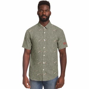 May include: Short-sleeved button-down shirt in a muted green color, featuring a repeating pattern of small airplanes and foliage. The shirt has a classic collar and is adorned with the red text "N2" on the sleeve.