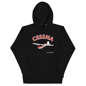 May include: Black hooded sweatshirt featuring a Cessna airplane graphic. The graphic includes the word "CESSNA" in red and white, along with the plane's design and the registration number N1234D. The sweatshirt has a front pocket and a drawstring hood.