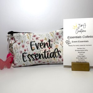 May include: A zippered pouch with a floral pattern in pink, green, and white, featuring the black text Event Essentials and a pink butterfly keychain. Beside it stands a white card with the text J and A Creations Essentials Colletion.