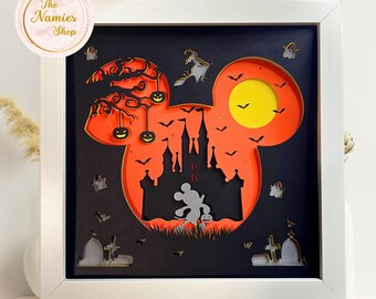May include: A framed Halloween-themed paper art piece. The artwork features a silhouette of Mickey Mouse's head with a castle, bats, pumpkins, and a full moon. The piece is in a white frame and includes the text "The Namies Shop".