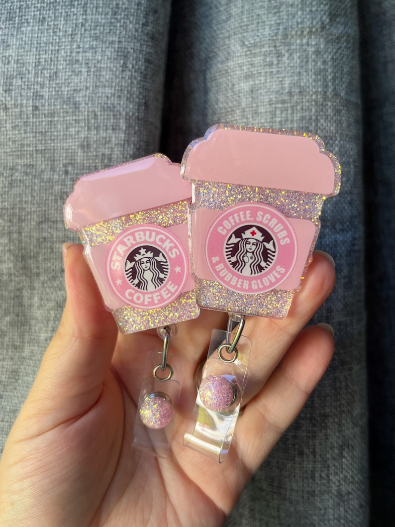May include: Two pink glitter coffee cup-shaped badge holders with a Starbucks logo and the text "Coffee, Scrubs & Rubber Gloves".