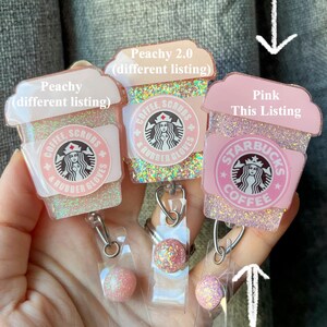 May include: Three pink and white glitter coffee cup themed retractable badge holders with a clear plastic badge holder and a pink glitter ball charm. The text on the cups reads "Coffee, Scrubs & Rubber Gloves" and "Starbucks Coffee".