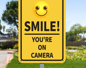 May include: Yellow sign with a smiling face and the text "SMILE! YOU'RE ON CAMERA".