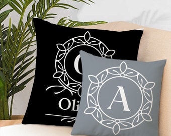 May include: Two decorative throw pillows with a black and grey background. The pillows feature a white monogram with a decorative border. The black pillow has the letter "O" and the word "Olivia" on it. The grey pillow has the letter "A" on it.