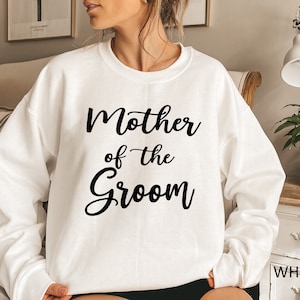 May include: White sweatshirt with the text "Mother of the Groom" in black cursive lettering.