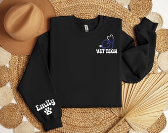 May include: Black sweatshirt with a white paw print and the name "Emily" on the left sleeve. The front of the sweatshirt has a blue stethoscope with a heart design and the text "VET TECH" in white.
