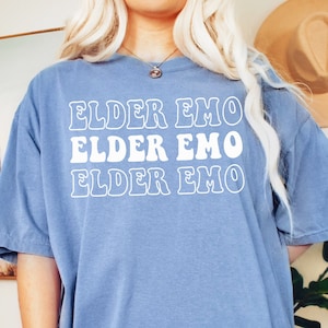 May include: A light blue oversized t-shirt with the text "ELDER EMO" repeated three times in white outlined letters.