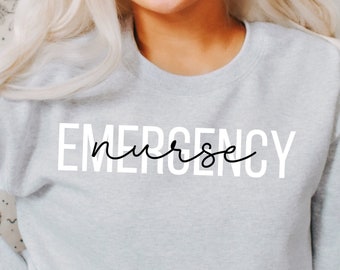 May include: A gray sweatshirt with the text "EMERGENCY nurse" printed in white on the front. The sweatshirt is being worn by a person with blonde hair. The text "color: ash" is visible in the bottom left corner of the image.