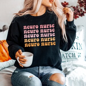 May include: A black sweatshirt with the text "neuro nurse" repeated five times in a pink and orange retro font.
