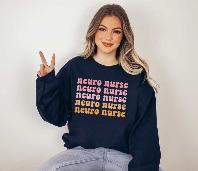 May include: A navy blue sweatshirt with the text "neuro nurse" repeated five times in a rainbow gradient. The text is in a retro font style.