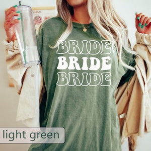 Pode incluir: Uma camiseta verde claro com a palavra "BRIDE" repetida tr&ecirc;s vezes em um estilo de fonte retr&ocirc;.