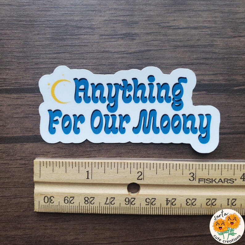 May include: A white sticker with the text "Anything For Our Moony" in blue, with a yellow crescent moon and stars. The sticker is approximately 3 inches long.