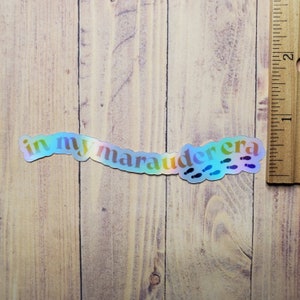 May include: A holographic sticker with the text "in my marauder era" and a trail of footprints.