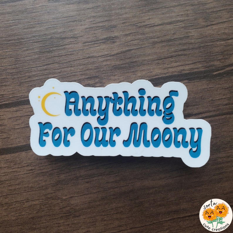 May include: A white sticker with the text "Anything For Our Moony" in blue, outlined in black. A yellow crescent moon and stars are above the word "Anything". The sticker has a rounded rectangular shape.