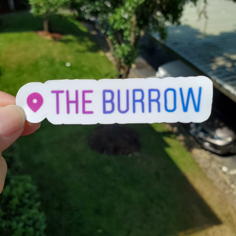 K&ouml;nnte beinhalten: Ein wei&szlig;er Aufkleber mit einem rosa und blauen Farbverlaufstext, der "THE BURROW" lautet, und einem rosa Standort-Pin-Symbol.