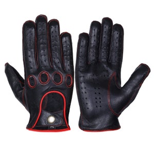 Puede incluir: Un par de guantes de conducir de cuero negro con costuras rojas. Los guantes tienen un diseño perforado y un cierre de botón en la muñeca.
