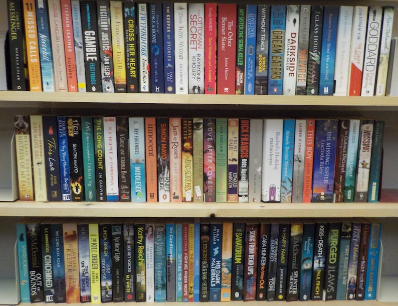 May include: A bookshelf filled with a variety of books, organized by color and genre. The books are arranged in three rows, with the top row containing mostly fiction, the middle row containing mostly non-fiction, and the bottom row containing a mix of both. The books are all in different sizes and shapes, and they are all in good condition.